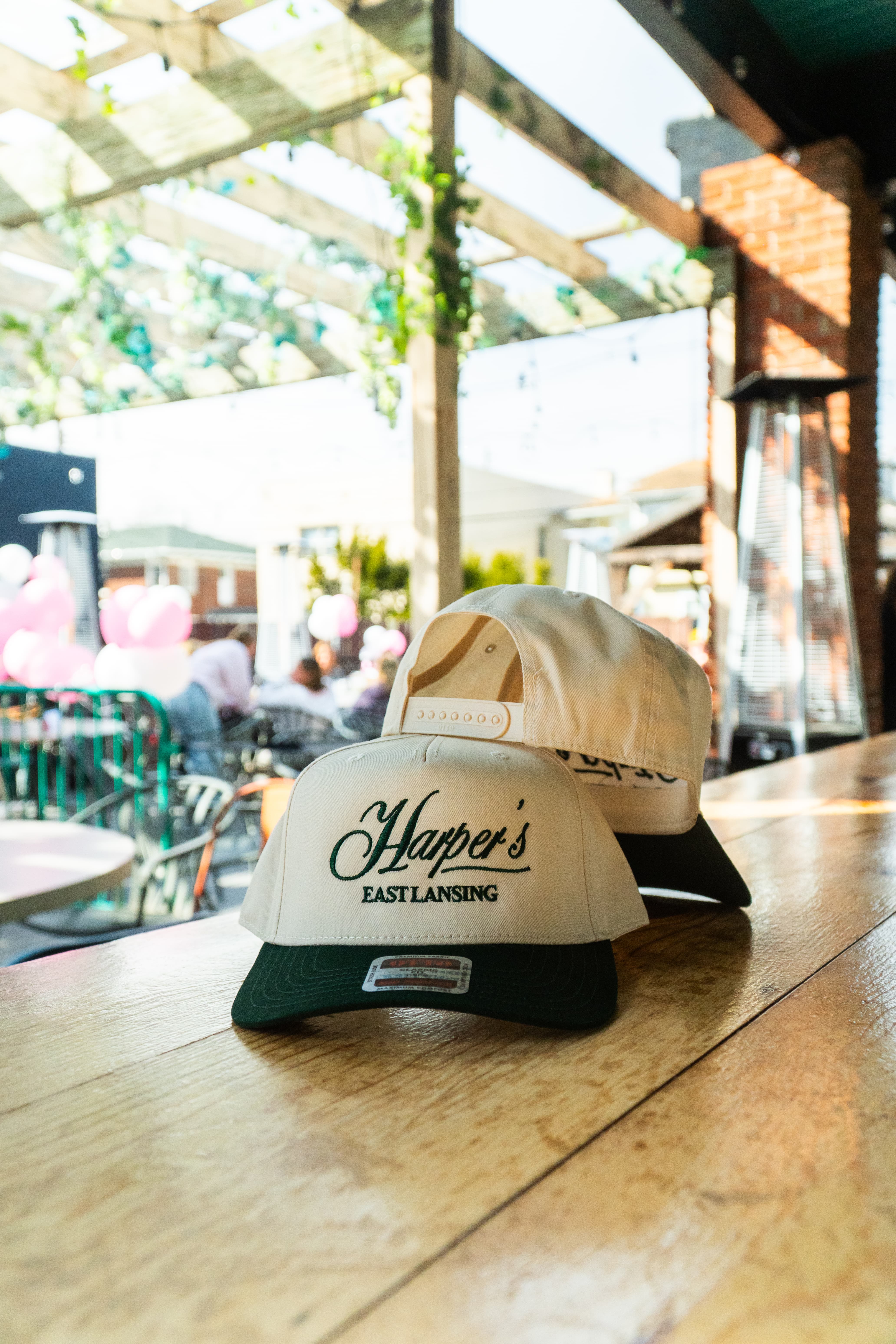 Harper's East Lansing hats on the patio table  cream and green, Est. 1997